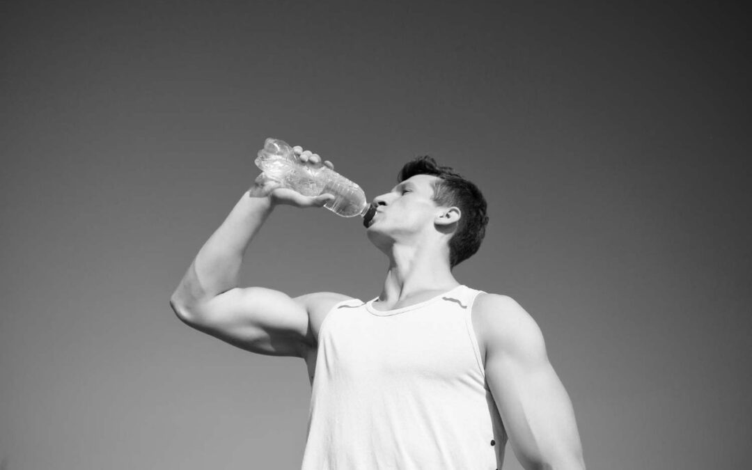 foto de un hombre musculado bebiendo un botellín de agua para hidratarse